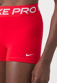 Red Nike Pro athletic shorts with a white logo and text on the elastic waistband. Smooth fabric, fitted design with minimal seams.