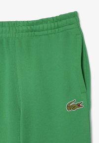 Gröna sweatpants med elastisk midja, sidofickor och en liten broderad krokodil-logotyp på vänster lår. Slät tygtextur.