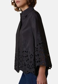 Blusa nera con colletto, maniche corte a sbuffo e ricami floreali intricati con dettagli a intaglio lungo l'orlo.