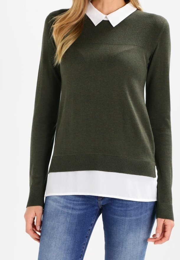 Olivgrön långärmad tröja med ribbad struktur, med en vit skjorta under. Kombinerad med blå jeans.