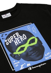 Camiseta de algodón negra con un estampado gráfico de un rostro con gafas verdes, fondo azul y un texto que dice "Soy un SUPERHEROE."