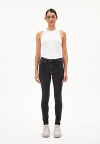 Witte geribbelde tanktop en zwarte skinny jeans. De stof ziet er glad uit; de jeans hebben een klassiek vijf-pocket ontwerp en subtiele stikdetails.
