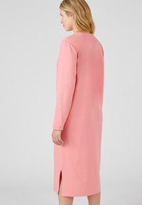 Abito di cotone rosa con maniche lunghe, scollo rotondo, spacchi laterali e dettagli decorativi sulle maniche. Silhouette semplice e dritta.