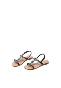 Sandali piatti neri con una soletta color nude, caratterizzati da un design di cinghie decorate con perline e cinturini alla caviglia regolabili. Texture liscia e punta aperta.