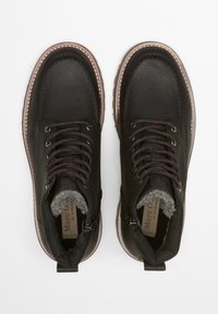 Schwarze Leder-Stiefeletten mit strukturiertem Finish, kontrastierenden dunklen Schnürsenkeln, gefüttertem Innenraum mit Fell und pinkfarbener Gummisohle mit Stitching-Details.