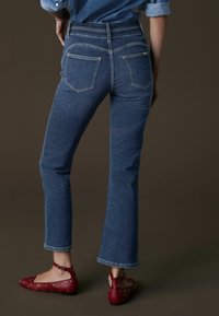 Blå jeans med midje höjd, utsvängd bensnitt och kontrasterande sömmar; matchade med röda lägenheter med ankelrem och metalliska nitar.