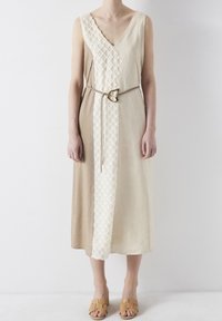 Vestido midi beige sin mangas con panel blanco texturizado, cinturón delgado con hebilla en forma de corazón, llevado con sandalias de tacón abierto en color tostado.