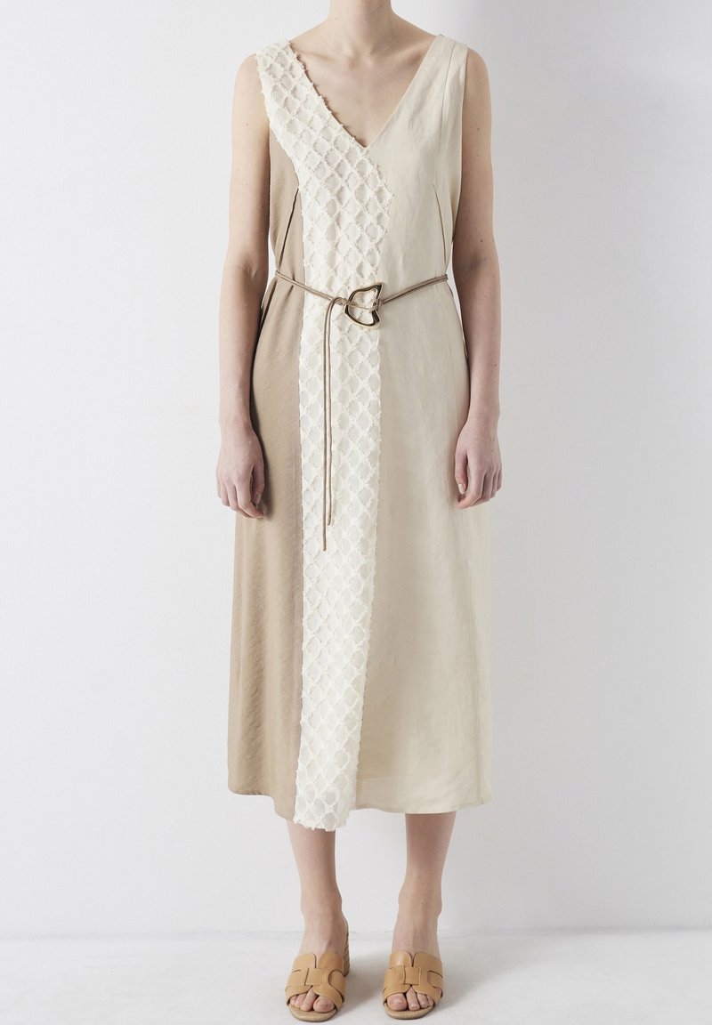 Vestido midi beige sin mangas con panel blanco texturizado, cinturón delgado con hebilla en forma de corazón, llevado con sandalias de tacón abierto en color tostado.