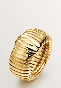 Pulsera en tono dorado con un diseño ondulado y estriado. Superficie lisa y pulida con secciones elevadas e hundidas alternas para dar textura. Forma redonda.