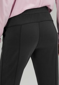 Svarta träningsbyxor med en slät yta, som har en bred elastisk midja och kontrasterande sömmar längs sidsömmarna.