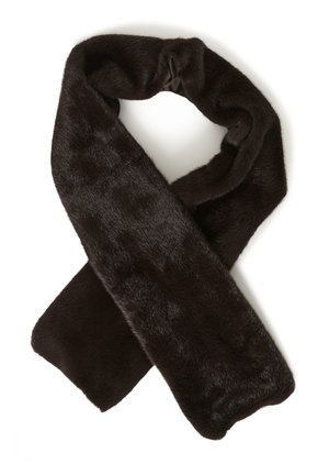 Femme portant un long manteau marron foncé, une écharpe en peluche assortie et un jean bleu foncé à jambes larges, debout devant un fond blanc uni.