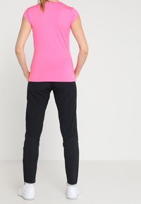 T-shirt med tight passform och korta ärmar i klar rosa, i kombination med svarta smala byxor. Båda plaggen är tillverkade av lätt och andningsbart tyg.