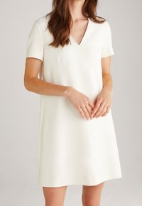 Weißes Kleid mit kurzen Ärmeln und V-Ausschnitt, glatte Textur, leicht ausgestellte Silhouette und dezente Nahtdetails in der Nähe des Oberkörpers.
