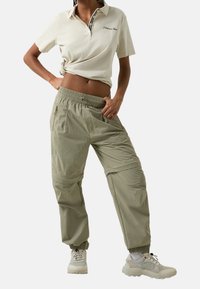 Polo beige avec col et rayure noire, associé à un pantalon cargo ample vert olive avec poignets élastiques et poches latérales. Baskets gris clair.