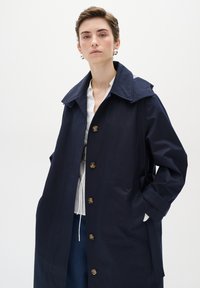 Tums zilā krāsā mēteli ar lielu apkakli, zeltītām pogām un sānu kabatām, izgatavots no gludas, vieglas auduma. Ikdienišķs, taisna griezuma dizains.