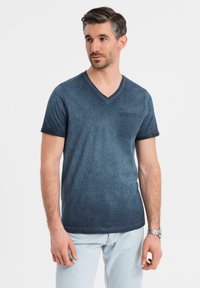 Námořnická modrá v-neck trička z jemné tkaniny s kapsou na levé straně hrudi, spárované se světle modrými džíny. Jednoduchý design a volný střih.
