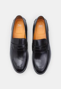 Mocasines de cuero negro con un acabado suave, que presentan una plantilla de cuero naranja y sin cordones visibles. Diseño simple con una forma suavemente curva.