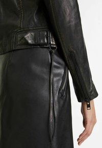 Veste en cuir noir avec une finition texturée, des poignets zippés et un détail de boucle de ceinture. Présente une silhouette lisse et élégante.