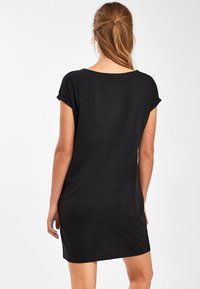 Robe en coton noir avec manches courtes retroussées, coupe ample et silhouette droite, dotée d'un décolleté arrondi et d'une longueur au-dessus du genou.