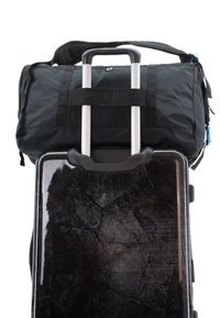 Black duffel bag with adjustable shoulder strap on top of a hard-shell suitcase featuring a textured black surface and silver zipper.