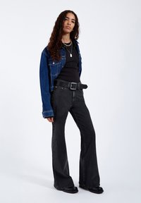Denim jacket in blue, black fitted t-shirt, and black flared jeans. Notable belt with a silver buckle and black platform shoes.