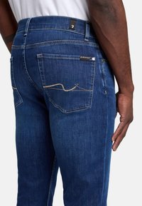 Ciemnoniebieskie dżinsy o prostym kroju z widocznymi szwami na tylnej kieszeni oraz nowoczesną metką w pasie.