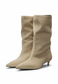 Beige suède enkellaarsjes met een slouchy ontwerp, puntige neuzen en een lage kittenhak. Glad textuur met minimale stikseldetails.