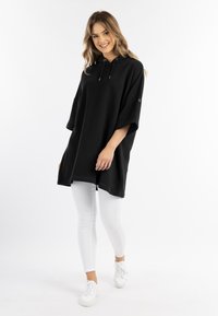 Rochie sweatshirt neagră, oversized, cu mâneci scurte, glugă cu șiret și buzunar tip cangur, asortată cu colanți albi și adidași.