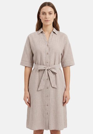 Donna che indossa un vestito beige al ginocchio con strisce bianche verticali, maniche corte, bottoni sul davanti e cintura di tessuto annodata in vita.