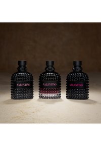 Three black studded Valentino perfume bottles with pink logo labels arranged side by side on a light surface against a dark background.