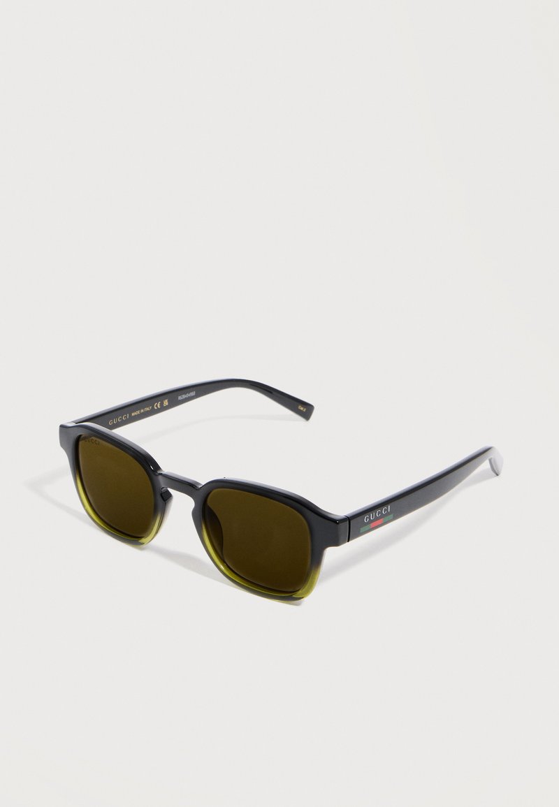 Lunettes de soleil Gucci dégradé noir et vert avec des verres rectangulaires marron et un logo sur la branche, présentées sur une surface blanche.