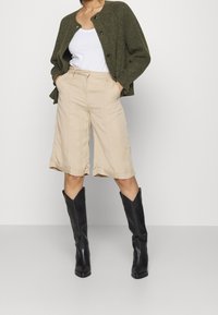 Grön stickad kofta, vit linne, beige cropped byxor med rullade fållar, svarta cowboystövlar med mönstrade detaljer.