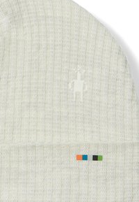 Gorro de punto en color crema claro con acanalado vertical. Presenta un logo texturizado en el mismo color y una franja de acento multicolor cerca del puño.
