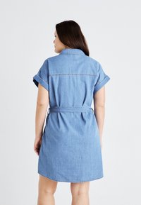 Denimkjole, lyseblå, kortermet med rullet opp ermer, innsvingt midje med belte, kne-length, bakfra, subtile sømdetaljer.