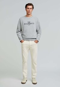 Grey sweatshirt with "THE SCALPERS CO." logo, paired with cream-colored pants and beige sneakers. Simple, relaxed fit design.