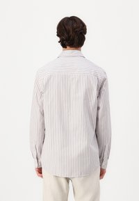 Chemise à manches longues boutonnée blanche avec de fines rayures verticales bordeaux. Dotée d'un col classique et de manches à boutons, fabriquée en tissu léger.