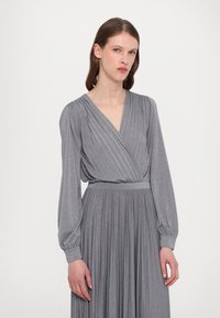 Robe grise à manches longues en tissu métallique, dotée d'un design enveloppant, d'une jupe plissée et d'une taille ajustée avec des manches froncées.