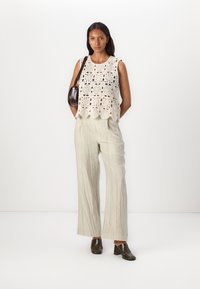 Crochet crop top v krémovej farbe s kruhovými vzormi, skombinovaný so svetlošedými plisovanými nohavicami a tmavými vysokými podpätkami. Hnedá kabelka.