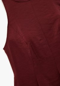 Top sin mangas burdeos con una tela texturizada y suave que presenta un brillo sutil, y detalles en las costuras a lo largo de los lados para un ajuste entallado.