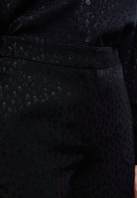 Tela negra con un sutil patrón en relieve de calaveras y estrellas. El material tiene una textura suave con botones a juego en la camisa.