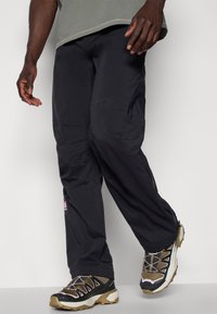 Musta, kevyet housut rentoa istuvuutta, joissa on pieni logo sivussa, ja ne on yhdistetty vaaleanharmaisiin ja mustiin urheilukengiin.