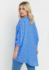 Blusa blu con stampa floreale, vestibilità ampia, spalla scesa e maniche a 3/4. Tessuto leggero con una consistenza liscia.
