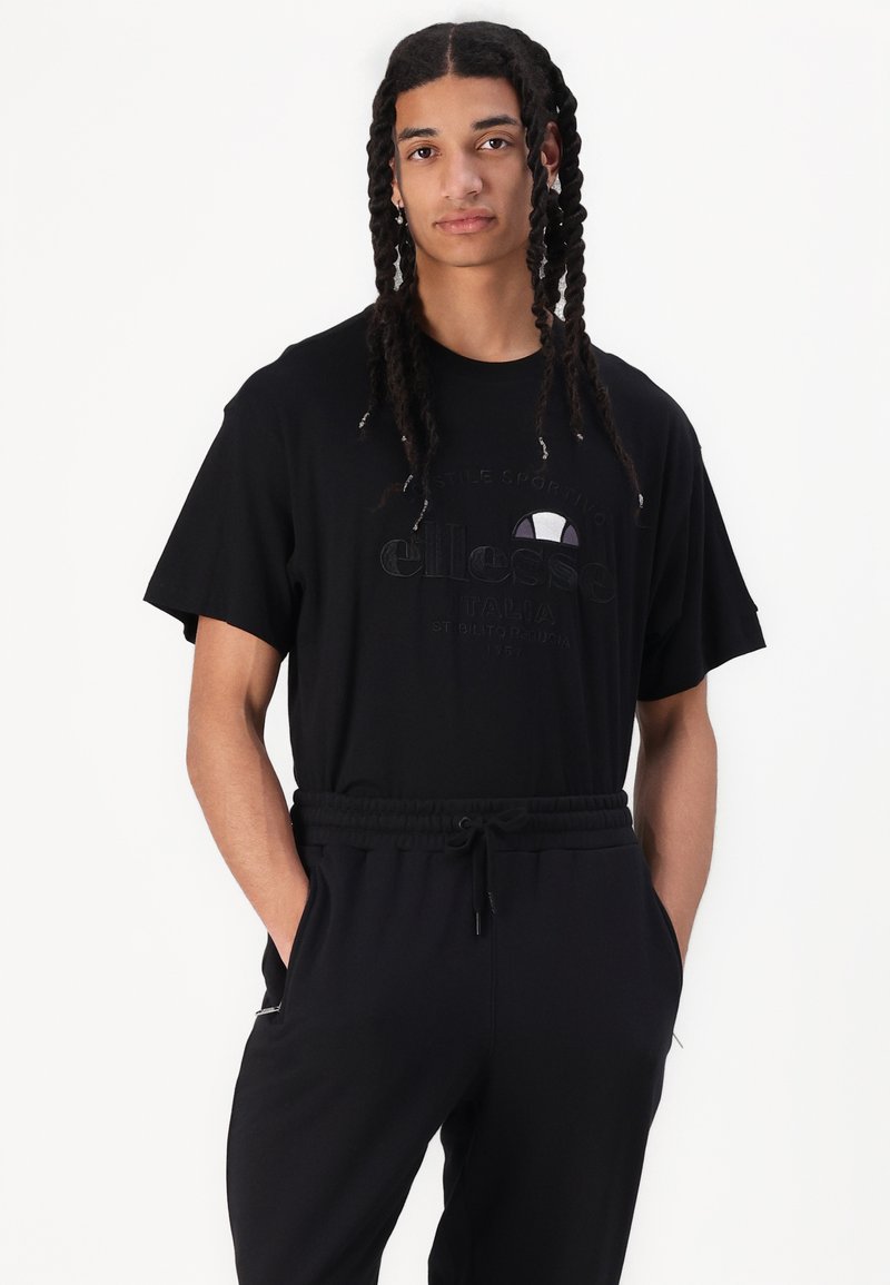 Czarna koszulka z krótkim rękawem, z teksturowanym nadrukiem logo. W połączeniu z czarnymi dresami, które mają elastyczną talię i boczne kieszenie.