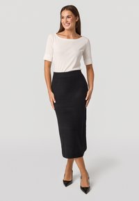 Jupe midi noire avec une silhouette ajustée et un motif texturé, associée à un haut crème clair à encolure bateau, complété par des escarpins noirs.