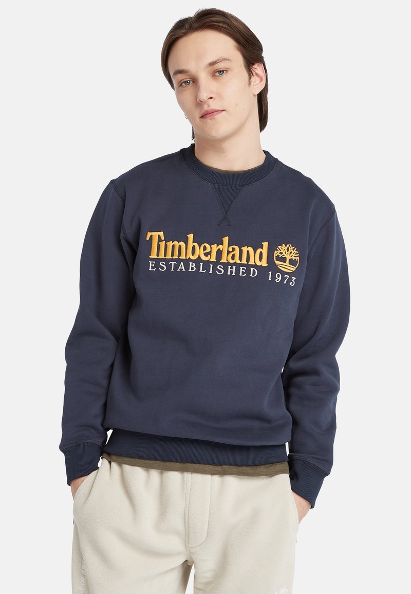 Felpa in cotone blu navy con collo a girocollo ribbed, con logo Timberland ricamato in giallo e data di fondazione sul davanti.