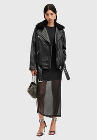 Μαύρο δερμάτινο μπουφάν μοτοσικλέτας με γούνα στον γιακά, μαύρο στενό φόρεμα με διαφανή φούστα, μεταλλικές γόβες και τσάντα με υφή.