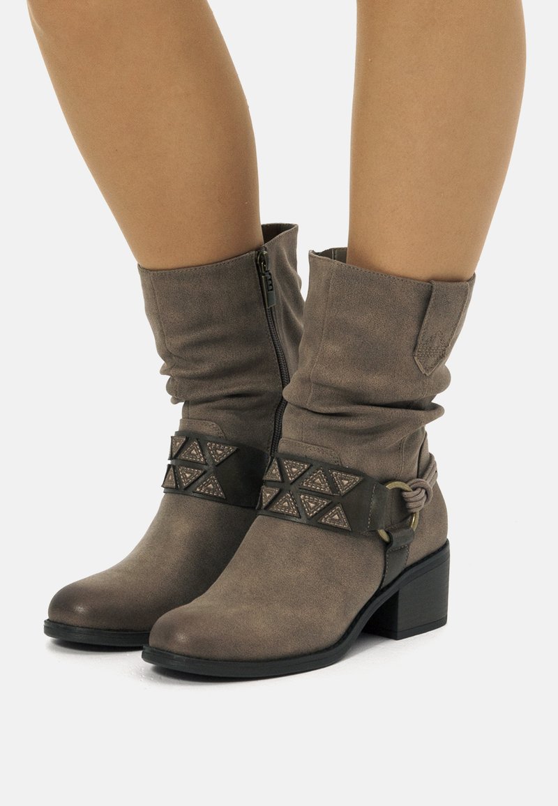 Botas de tobillo en taupe con un diseño arrugado, que cuentan con una banda decorativa con acentos triangulares, cierre con cremallera y un tacón grueso.