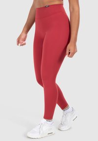 Red high-waisted leggings made of stretch fabric, featuring a smooth texture. Paired with white athletic shoes and socks.