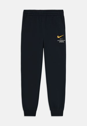 Czarne spodnie dresowe Nike z elastycznym pasem i ściągaczami, z małym pomarańczowym swooshem Nike oraz białym napisem na lewej nogawce.