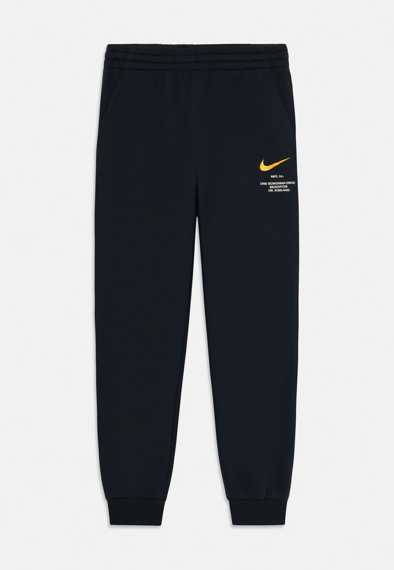 Černé Nike tepláky s elastickým pasem a manžetami, s malým oranžovým logem Nike a bílým textem na levém stehně.